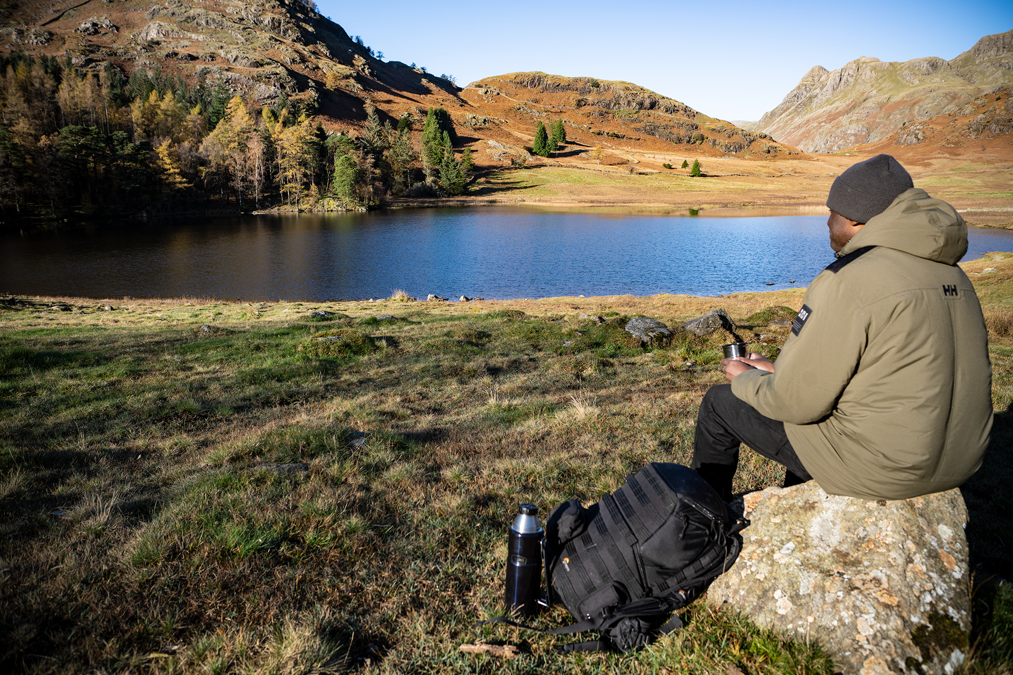 A seated walker holding a cup and looking across a lake towards sunlit hills