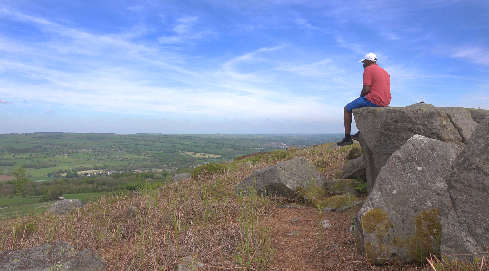 Gary sitting on a rock at Cow and Calf Rocks on Ilkley Moor, looking across the countryside beneath a blue sky
